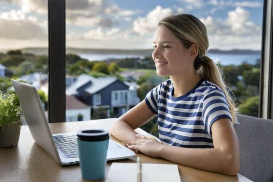 Young woman online at desk overlooking Australian suburb