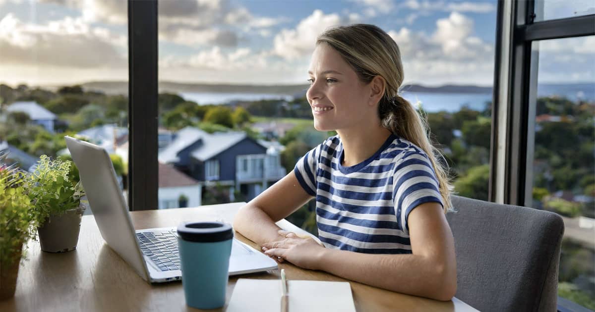 Young woman online at desk overlooking Australian suburb